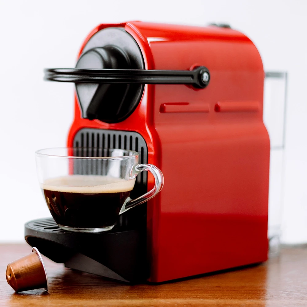 red domestic coffee machine with pods and half full glass coffee cup