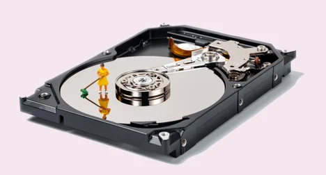 a close up of a hard drive with the casing open and a tiny figure with a broom sweeping the hard disk itself