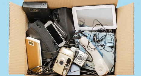 Top view of an open cardboard box full of old electrical items against a bright blue background.